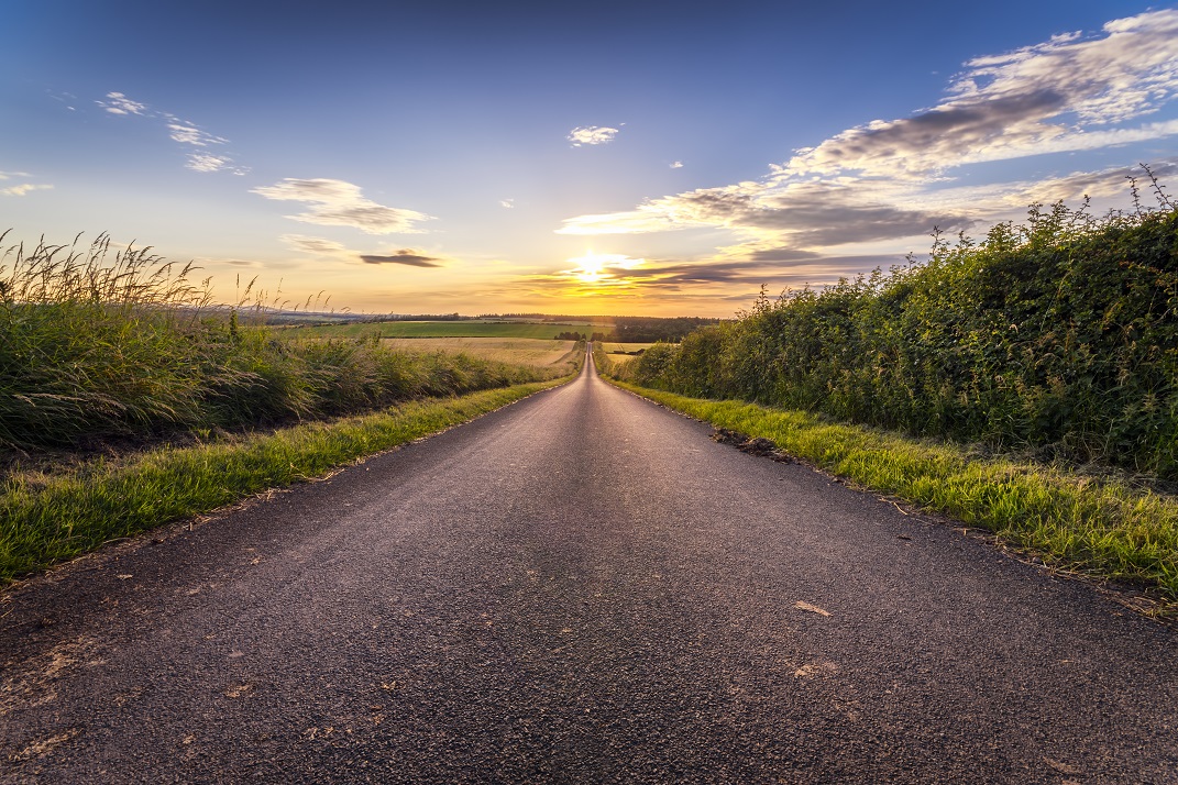 Country road leading to sunset on horizon