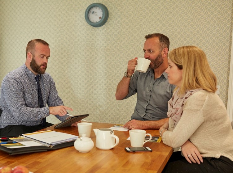 Adviser discussing documents with a couple seated at a table with coffee mugs.